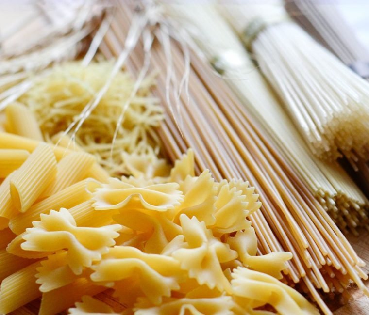 Close-up of different uncooked pasta varieties including spaghetti, rigatoni, fettuccine, and farfalle.