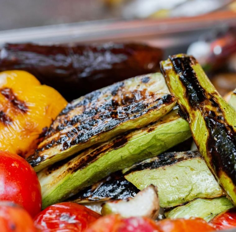 Close-up of assorted grilled vegetables including zucchini, peppers, and tomatoes with char marks.
